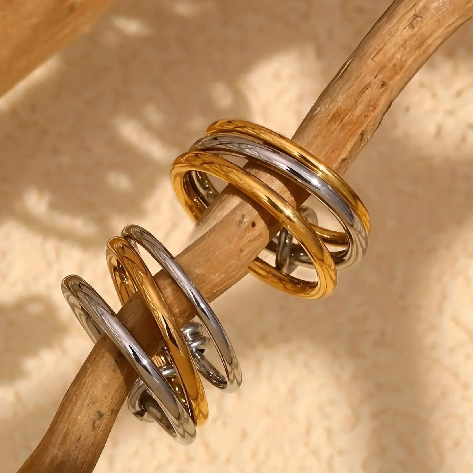 18K yellow gold and silver dual-tone interlocking stackable rings close-up oblique view on wooden twig warm natural lighting detail shot