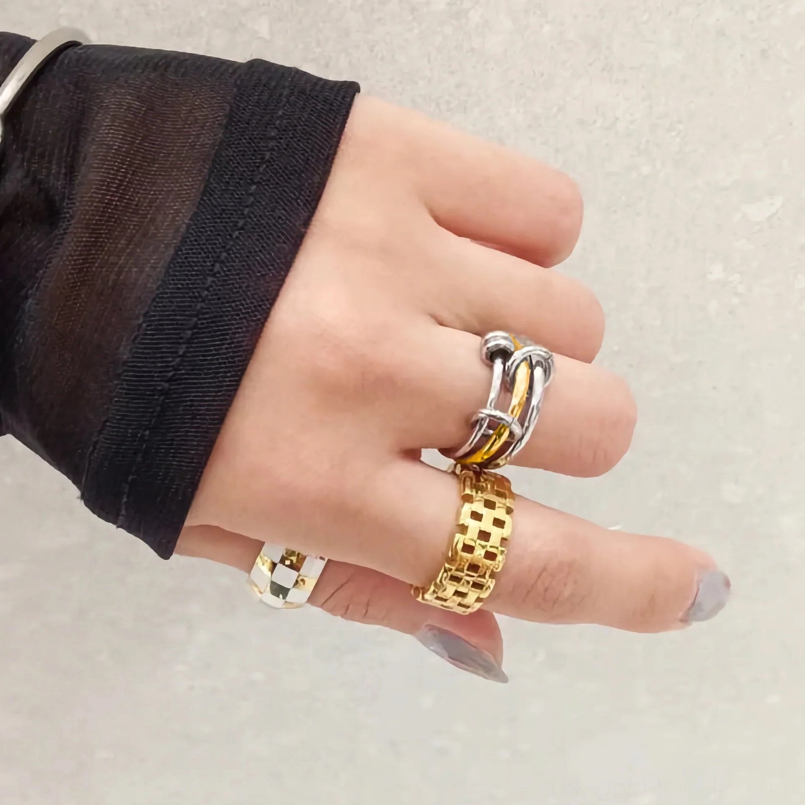 hand model wearing 18K gold two-tone stacked rings on multiple fingers with black sheer sleeve showing layered ring styling versatility