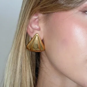 18K gold earrings worn on model's ear, close-up portrait showing conical stud design and lustrous gold plating