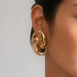 Close-up side view of 18K gold interlocking hoop earrings worn on female ear demonstrating chunky curved design and high-polished gold finish