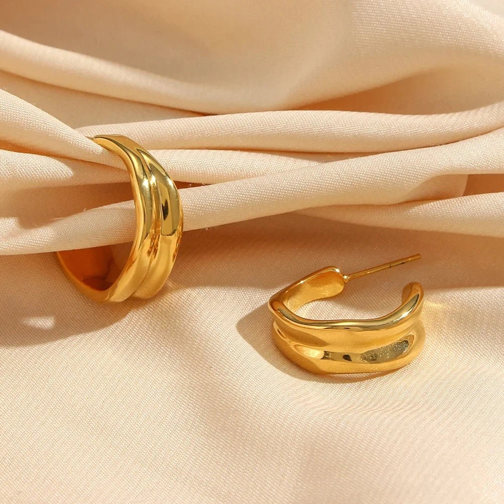 18K gold wave hoop earrings oblique angle flat lay on beige silk fabric luxury presentation