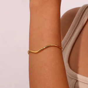 Gold wavy cuff bangle bracelet worn on female model arm close-up side view sleek polished finish