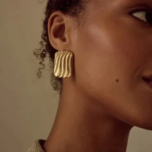 18K gold wavy ribbed rectangular stud earrings worn on ear model close-up side view