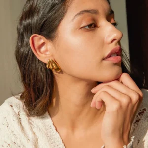18K gold wing earrings worn on model ear side profile lifestyle shot warm lighting