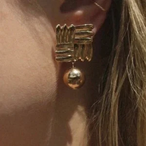 18k gold geometric drop earrings worn on ear - close-up side view showing woven stud and dangling gold bead