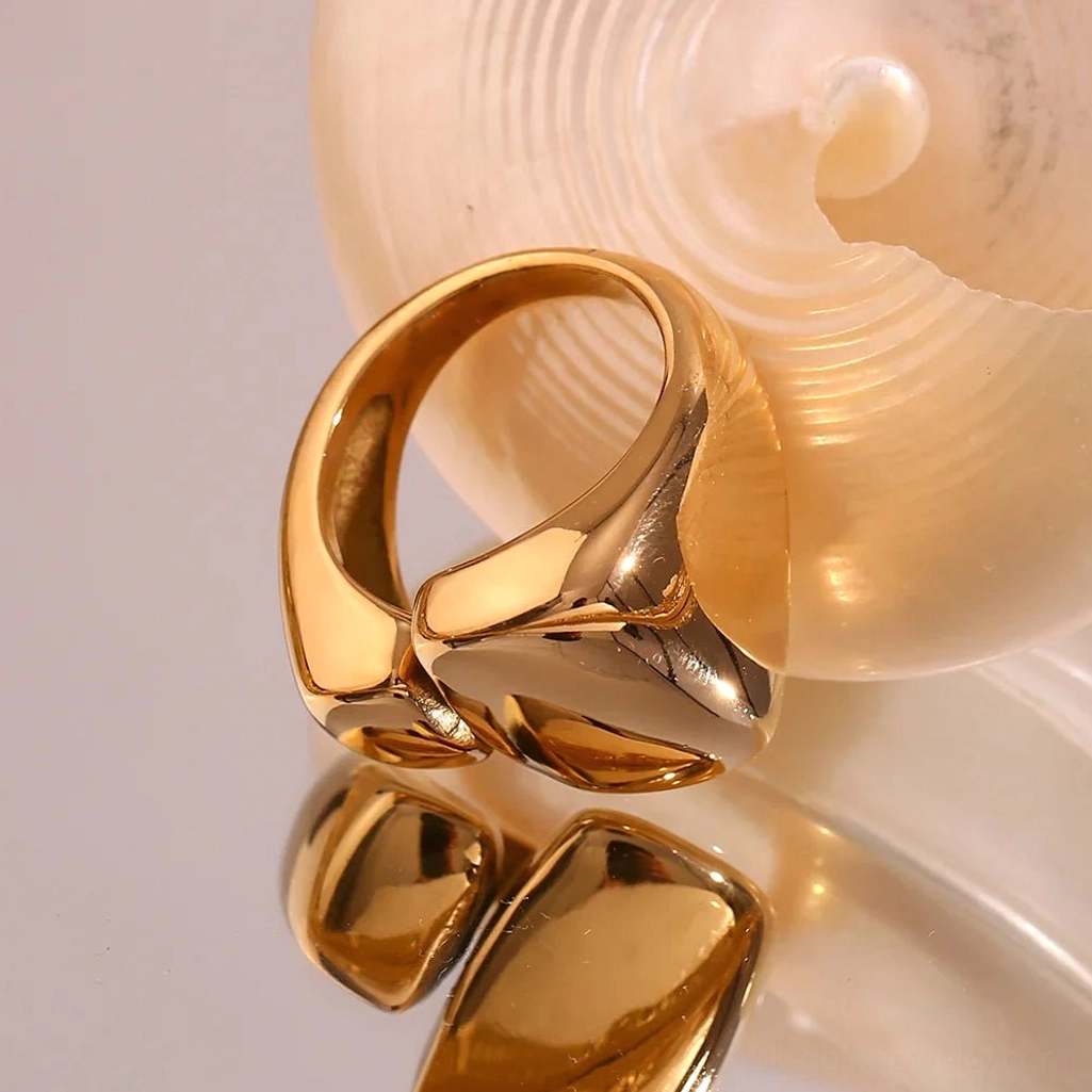 18K Gold wrap geometric ring with high-shine finish on seashell decorated background, angled side flat lay showing smooth chunky architectural design
