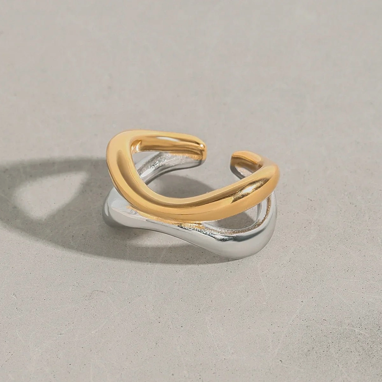 18K two-tone intertwined open ring front view, gold and silver layered curved design on gray background