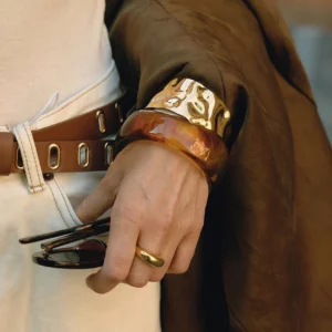 Woman wearing stacked chunky amber marbled acrylic bangle with gold metal cuff on wrist close-up
