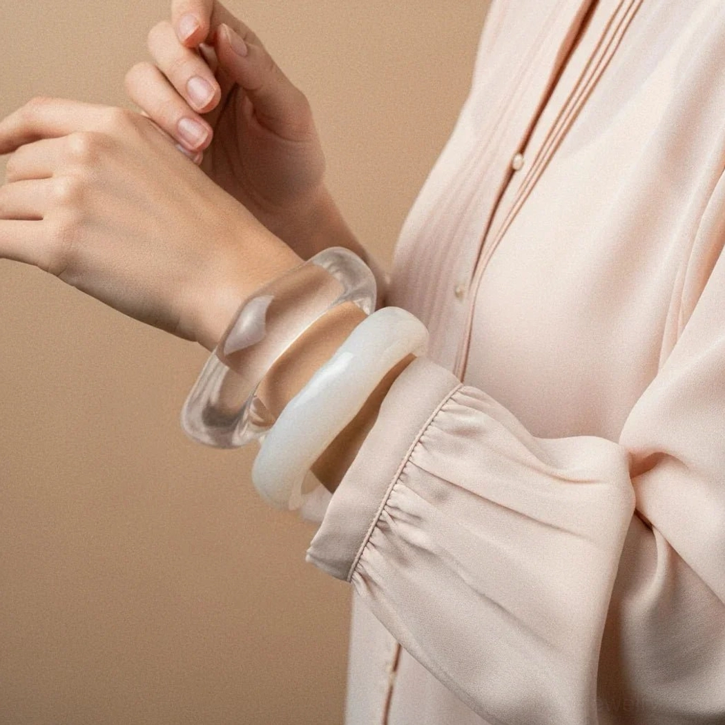 Clear transparent and off-white opaque acrylic bangles worn on model wrist, side view with light blouse and soft studio background