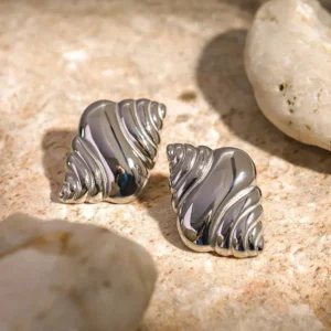 Pair of silver conch stud earrings showcasing textured spiral ridges on natural stone surface with pebbles - close-up detail