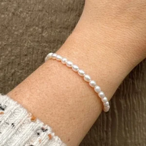 Freshwater pearl bracelet worn on wrist - close-up side view showing slim pearl strand fitted elegantly on adult wrist with knit cuff, demonstrating comfortable fit and versatile styling