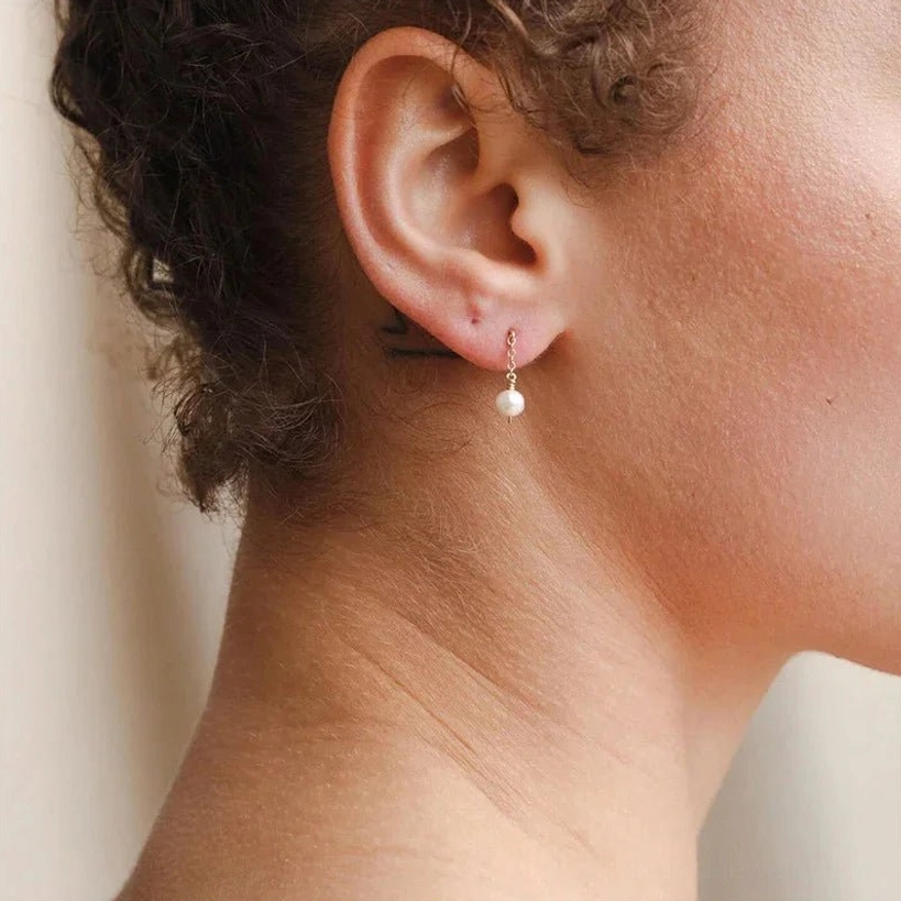 Minimal freshwater pearl drop earrings back view close-up showing tiny round white pearl and gold-toned metal fitting on female ear
