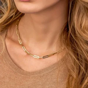 Gold paperclip chain necklace worn on female model with light brown wavy hair showing asymmetrical mixed link design close-up