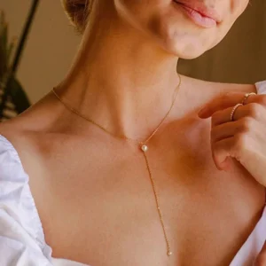 Gold pearl lariat necklace worn on model with white ruffled sleeve, showing Y-drop design with matching gold accessories on chest