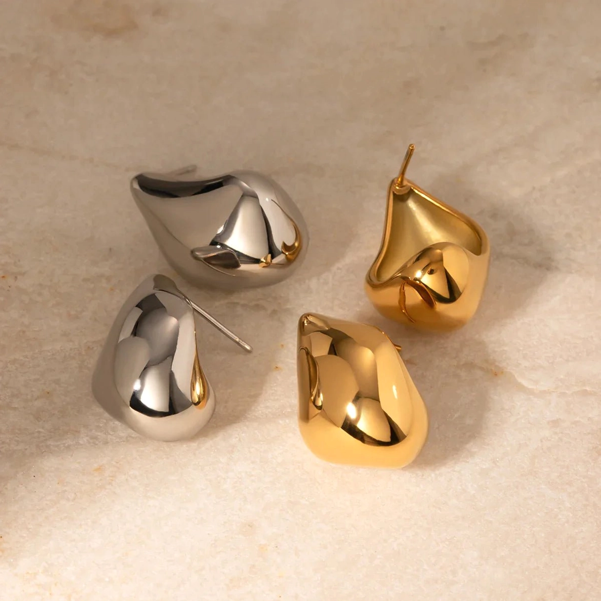 Gold and silver teardrop stud earrings comparison marble background mixed metals