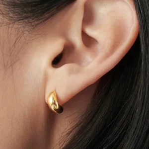 Close-up side view of gold huggie earrings on model ear showing glossy gold finish secure fit