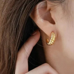Woman wearing gold twisted croissant hoop earrings close-up side ear view with hand in hair