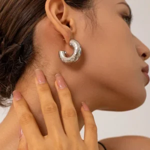 Silver hammered hoop earrings worn on model ear studio close-up showing artisan texture and shine on earlobe