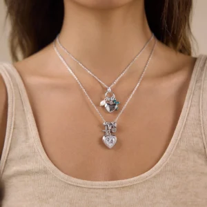 Layered multi-charm heart necklaces on female model - silver pendant with pearl and cross accents