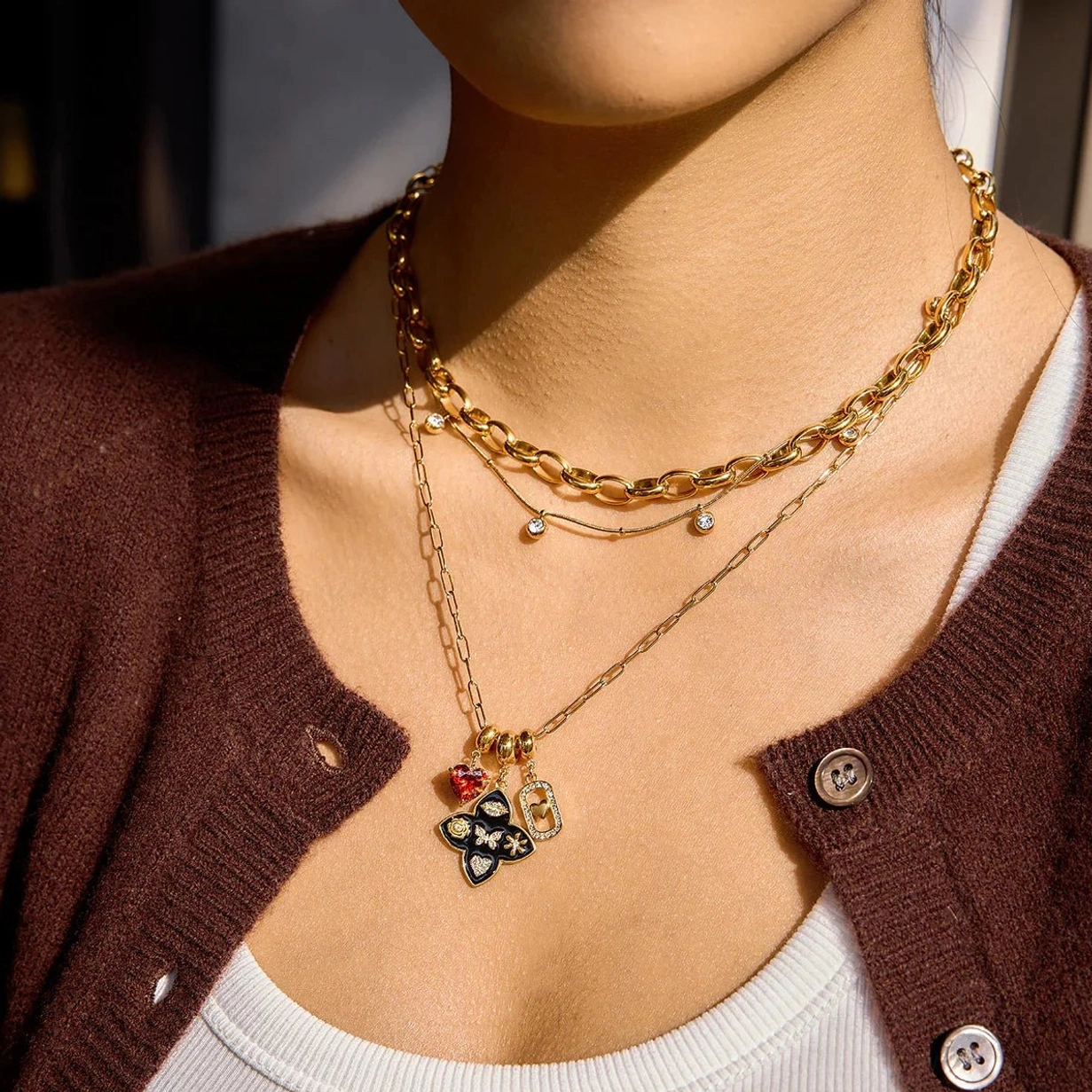 layered 18k gold necklace set on female model wearing brown cardigan and white top upper body view