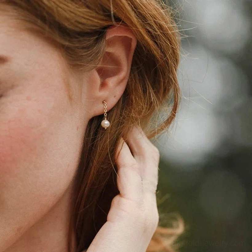 Pearl dangle stud earrings outdoor side profile view on female model with light brown hair showing casual styling and delicate pearl design