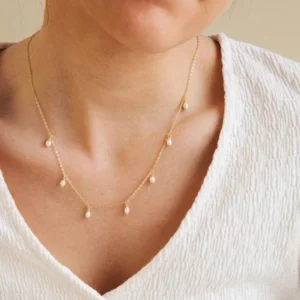 Dainty pearl station necklace worn on model neck close-up shot with white V-neck top showing delicate gold chain