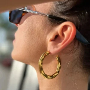 Riley gold hoop earrings worn on model ear side close-up outdoor setting glossy gold finish