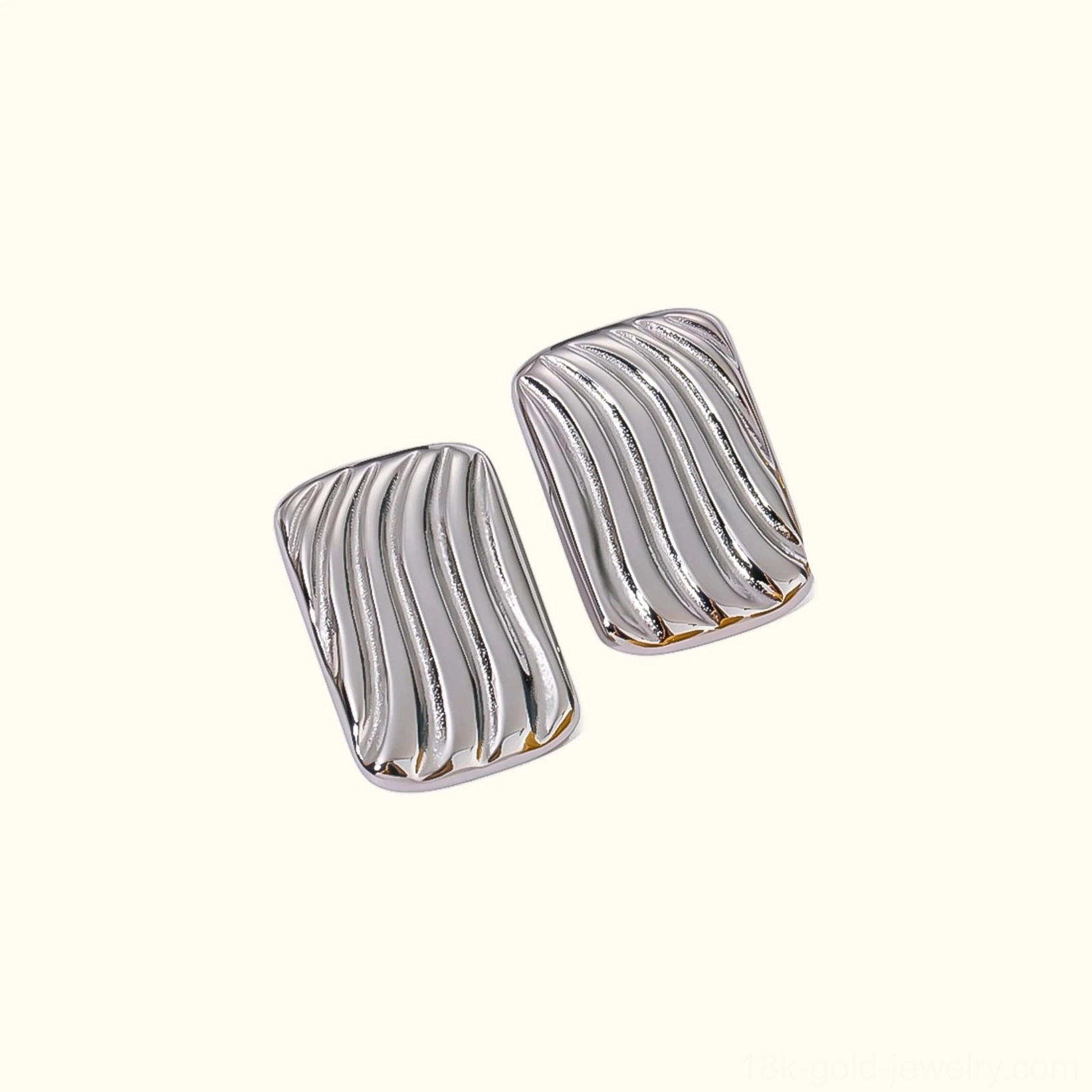 Silver wavy rectangular stud earrings angled view fabric background luxury earrings