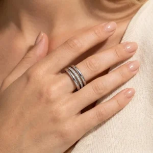 Stacked diamond rings worn on model's index finger, overhead close-up shot showing polished silver finish and diamond pavé detail against beige knit fabric