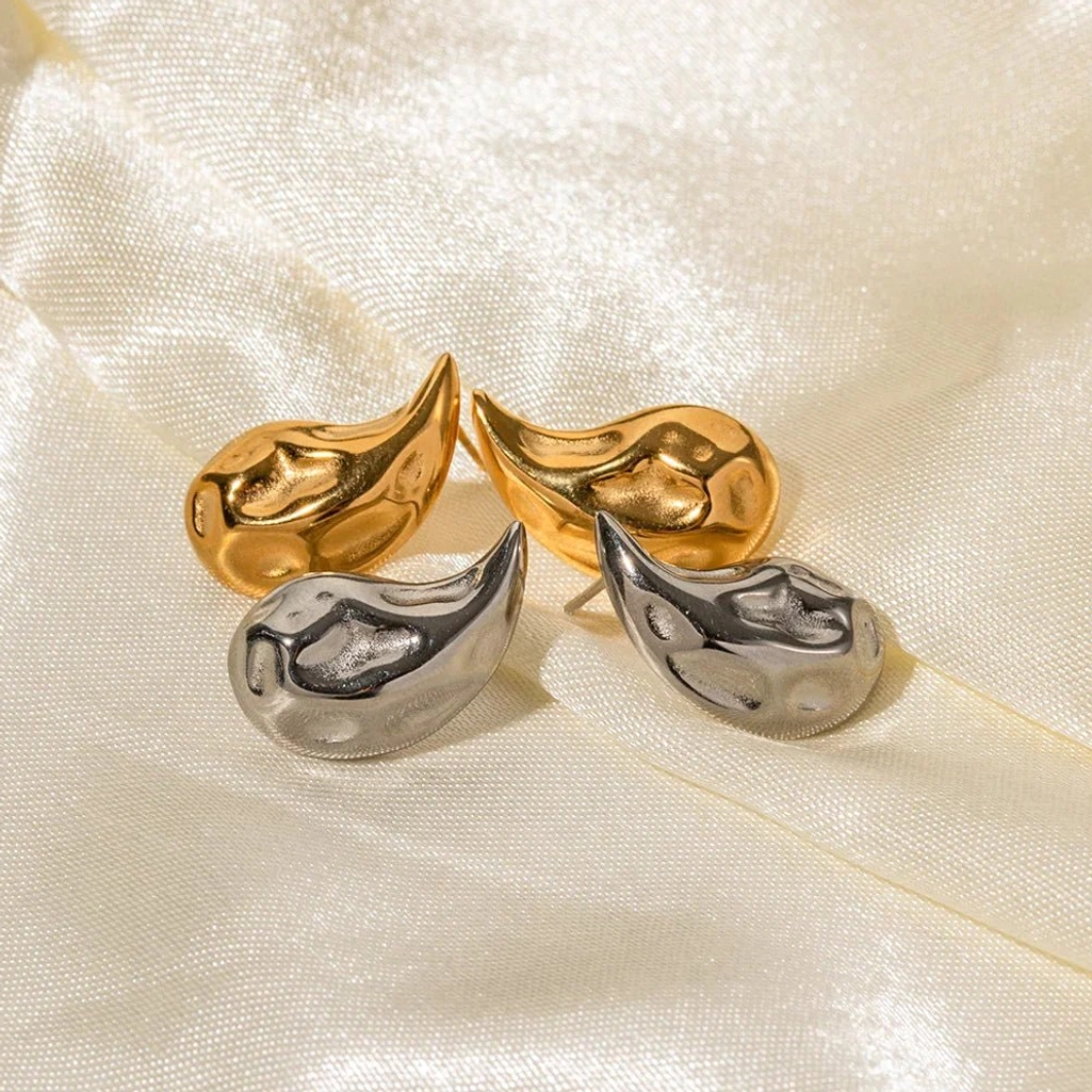 Mixed metal teardrop earrings collection with gold and silver pieces on satin fabric, angled view showcasing elegant irregular polished shapes